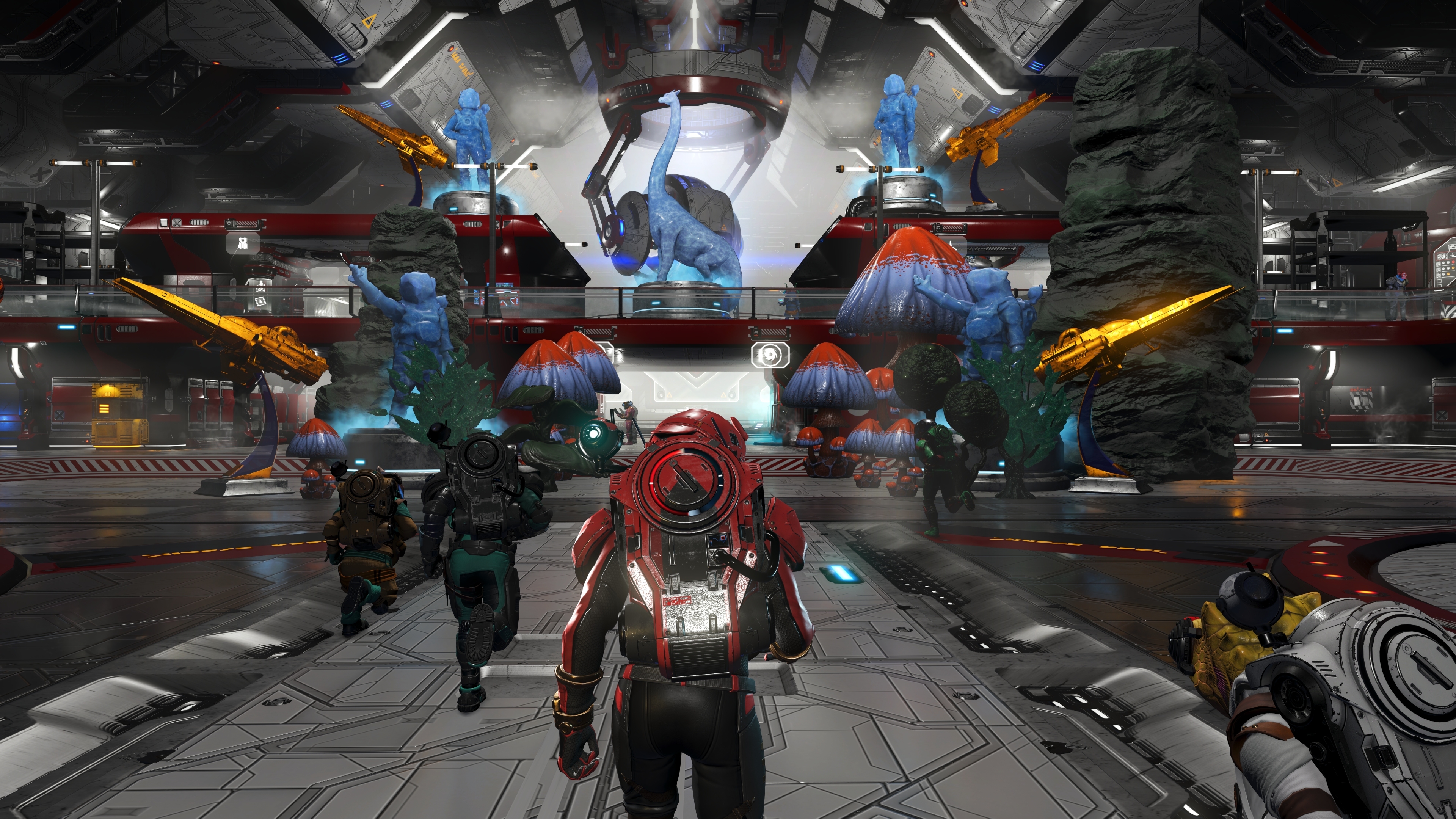 Players walk through a No Man's Sky space station concourse decorated with statues, gold ship sculptures and alien flora.